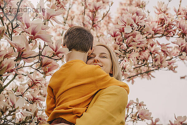 Smiling mother carrying son by blossoming magnolia tree in garden