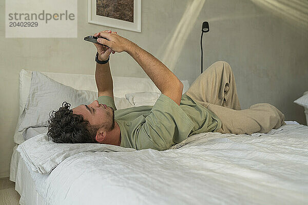 Young man using mobile phone on bed at home