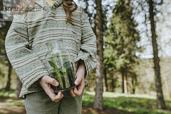 Girl holding glass bottle with plants in forest