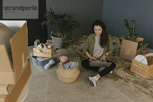 Woman using laptop sitting amidst boxes in new home