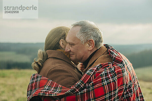 Happy senior couple hugging each other with tartan blanket under sky