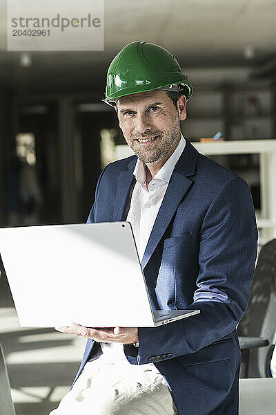 Mature engineer wearing hardhat using laptop sitting on desk in office