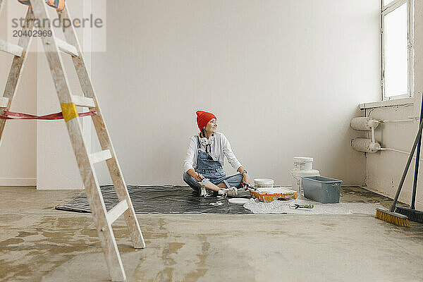 Woman sitting near paint equipment in front of white wall in new apartment