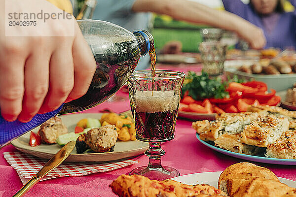 Hand of man pouring cold drink into glass at table