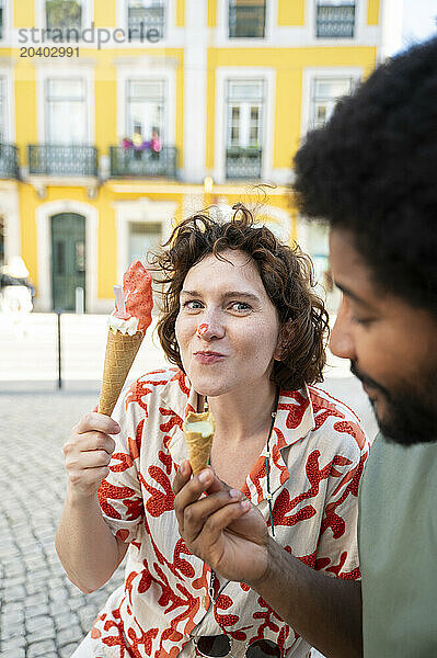 Playful woman eating ice cream with friend at street