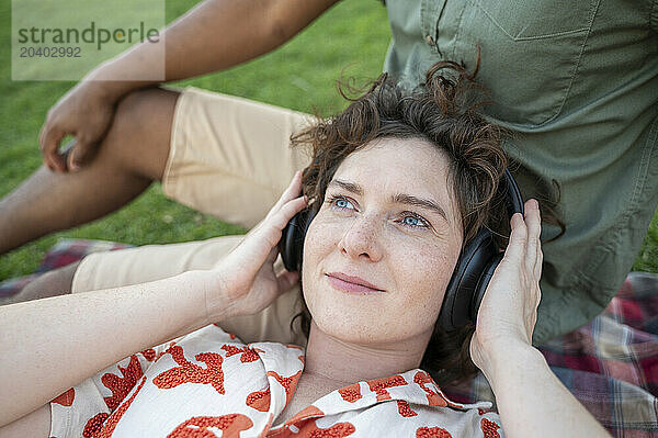 Smiling woman listening to music through wireless headphones and lying down on boyfriend's lap