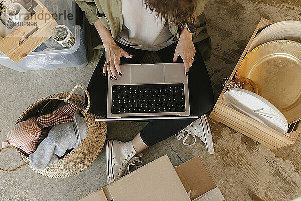 Woman using laptop sitting amidst boxes in new apartment