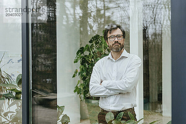 Businessman standing with arms crossed seen through glass