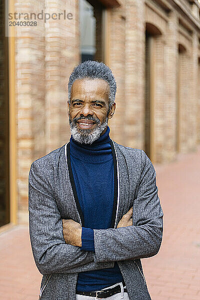 Happy businessman standing with arms crossed in front of building