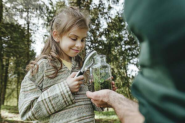 Girl and father with plant in glass bottle at forest