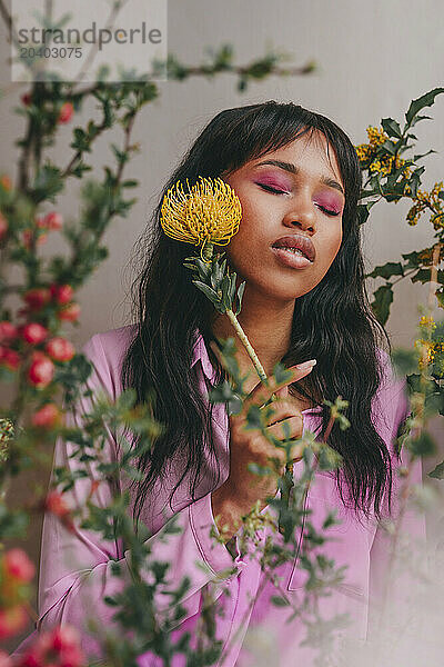 Woman with eyes closed touching Leucospermum flower on face