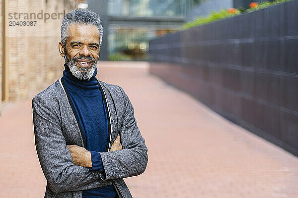 Smiling mature businessman standing with arms crossed on footpath