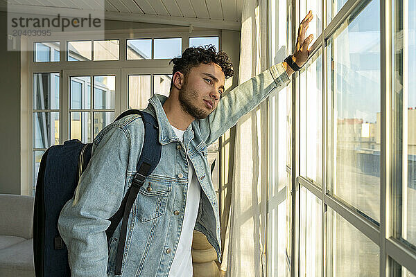 Young man standing with backpack near window at home