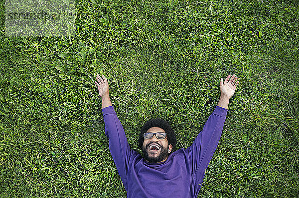 Smiling man with arms outstretched lying on green grass in lawn