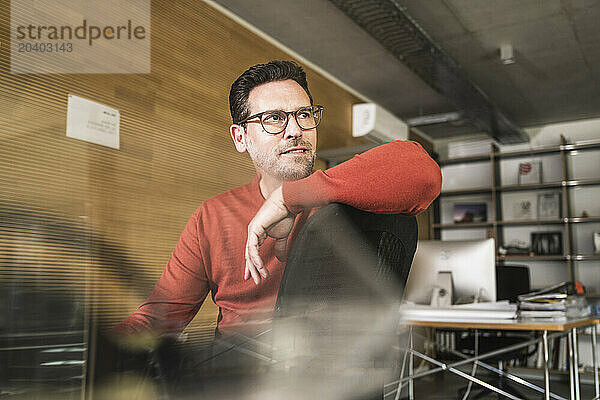 Thoughtful businessman looking away sitting on chair in office