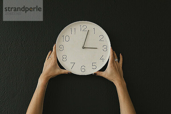 Hands of woman holding wall clock against black background