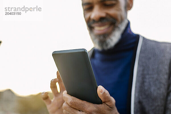 Smiling businessman using smart phone under sky