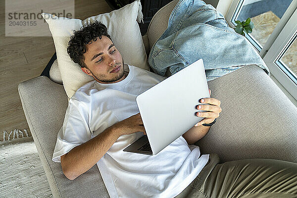 Young man using laptop on sofa at home