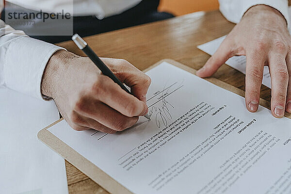 Businessman signing agreement with pen at desk in office