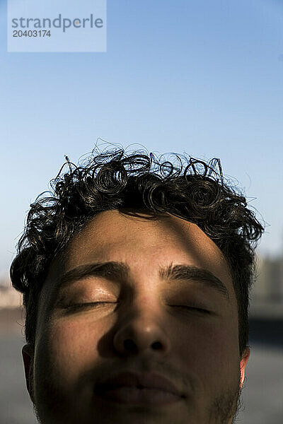 Young man with eyes closed and sunlight over face