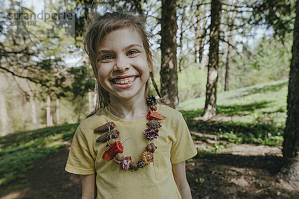 Smiling girl wearing natural necklace standing in forest