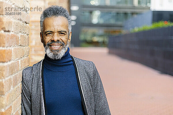 Smiling mature businessman leaning on wall at office park