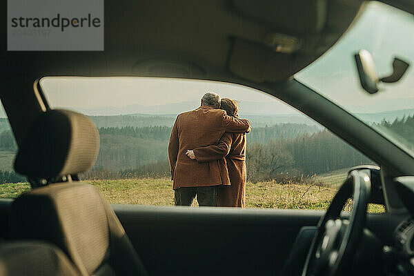 Happy senior couple hugging each other seen through car window