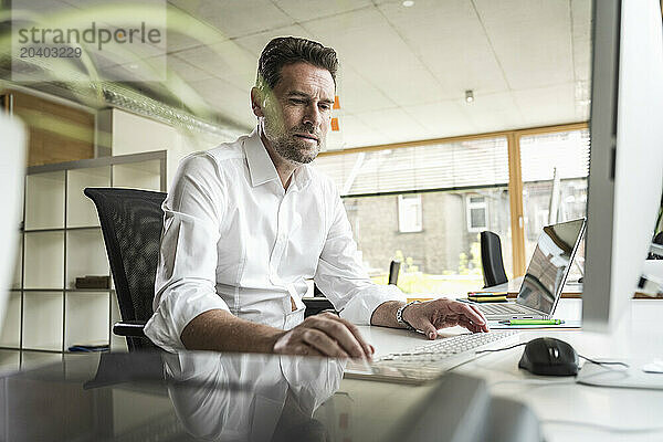 Mature businessman using computer sitting at desk in office