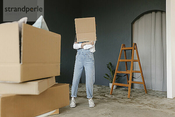 Woman with arms crossed covering face from box in new home