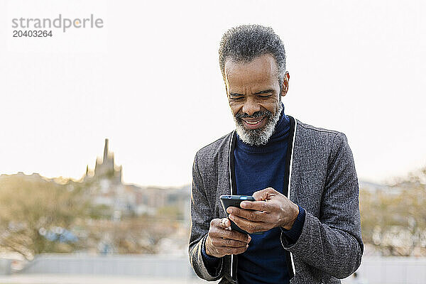 Happy businessman using mobile phone under clear sky