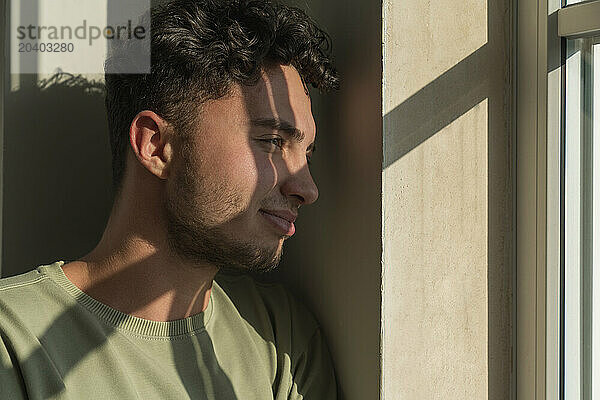 Thoughtful young man looking through window