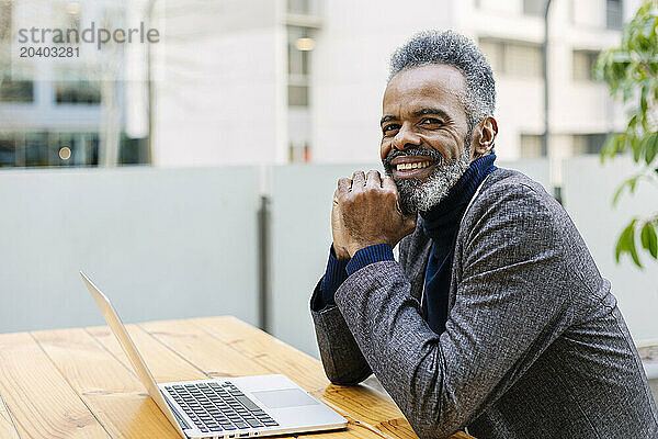 Happy businessman sitting with laptop at table