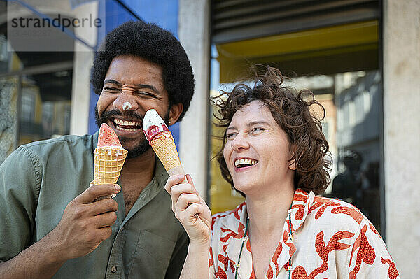 Cheerful couple having fun with ice cream cones near building