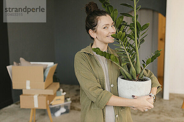 Smiling woman carrying potted plant standing in new apartment