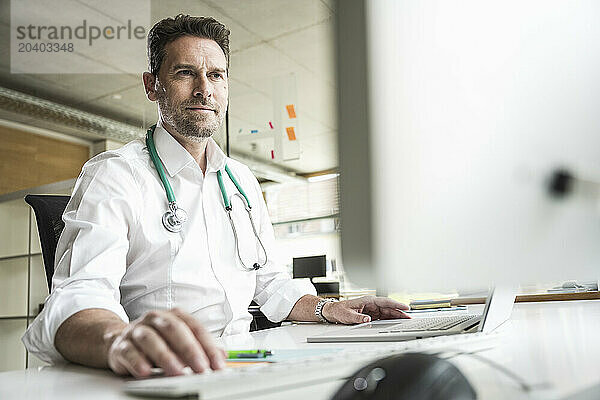 Confident doctor using computer at desk in office