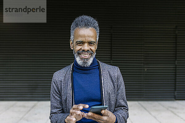 Happy businessman with smart phone in front of black wall