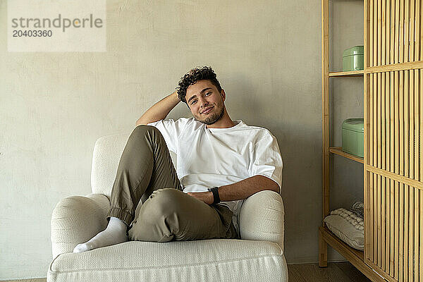 Smiling young man sitting on armchair at home