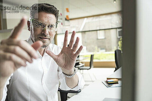 Confident businessman gesturing and wearing smart glasses sitting at office