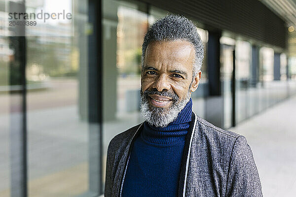 Smiling mature businessman with gray hair near building