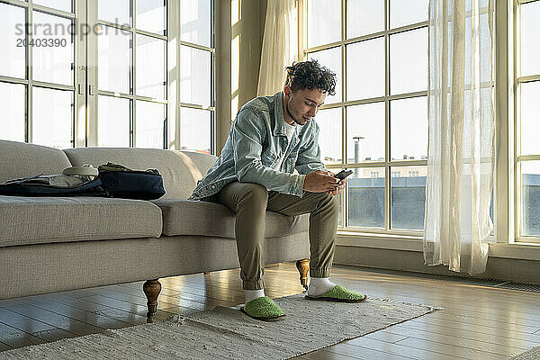 Young man using mobile phone on sofa at home