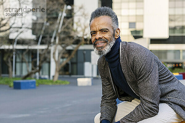 Smiling businessman sitting near building in office park