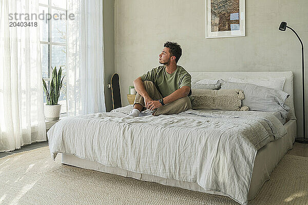 Thoughtful young man sitting on bed at home