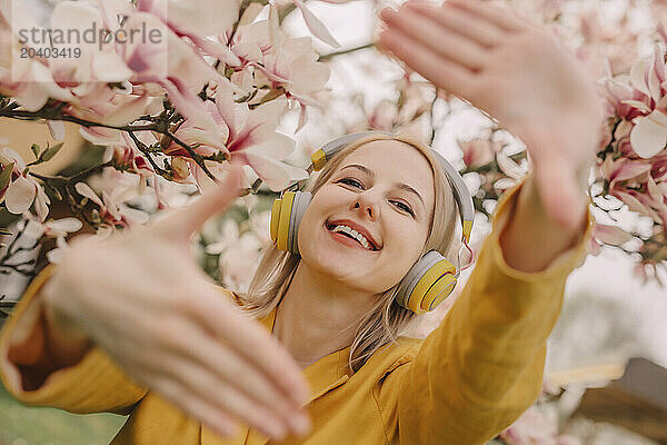 Happy woman listening to music through wireless headphones gesturing by magnolia tree in garden