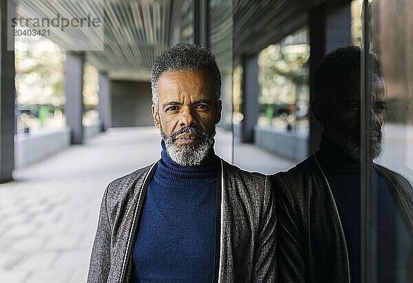 Mature businessman leaning on glass at footpath