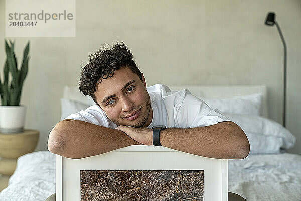 Smiling man sitting with picture frame on bed at home