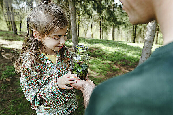 Girl and father with plant in glass bottle at forest