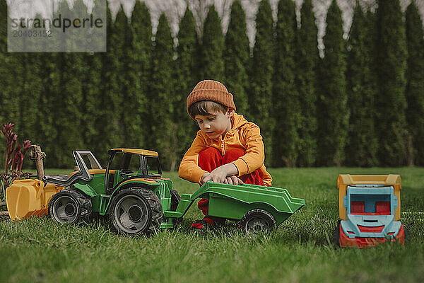 Boy crouching and playing with toy tractor on green grass in back yard