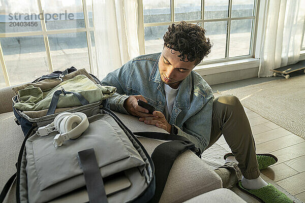 Young man using smart phone near sofa at home