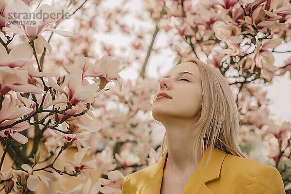 Blond woman with eyes closed by magnolia tree in garden