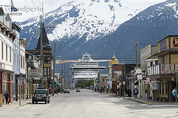 Cruise ships are seen docked at the Port of Skagway in southern Alaska. Large mountains adorn the landscape and make a scene that is magnificent to behold. This is looking down main street at the port with a large cruise ship docked.